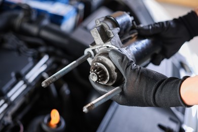 Photo of Auto part. Professional mechanic with starter motor near open hood of car indoors, closeup