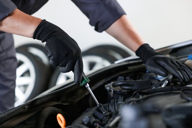 Photo of Auto parts. Professional mechanic with screwdriver fixing car indoors, closeup