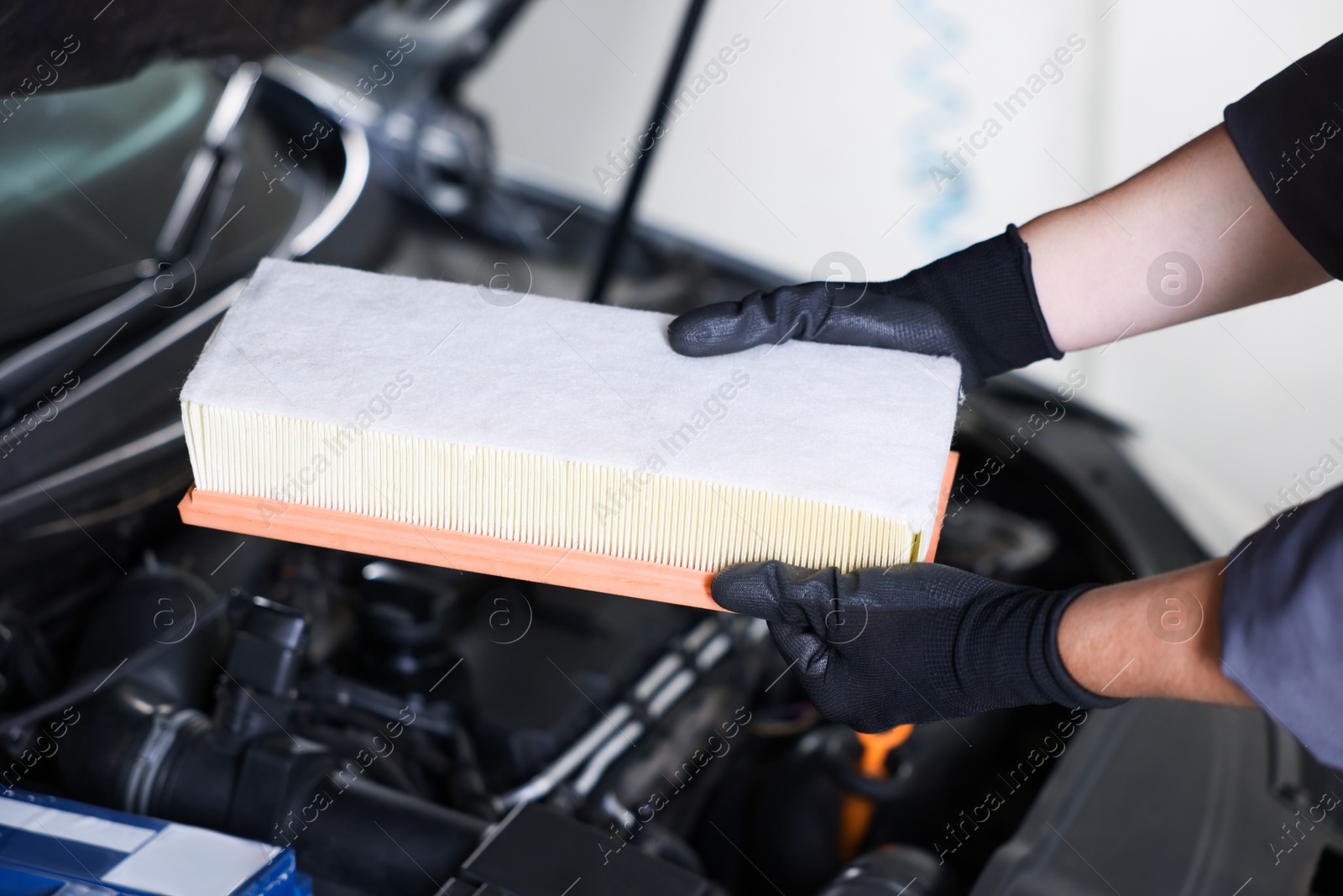 Auto part. Professional mechanic with air filter near open hood of car indoors, closeup Photo of Auto part. Professional mechanic with air filter near open hood of car indoors, closeup