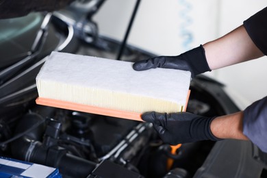 Photo of Auto part. Professional mechanic with air filter near open hood of car indoors, closeup
