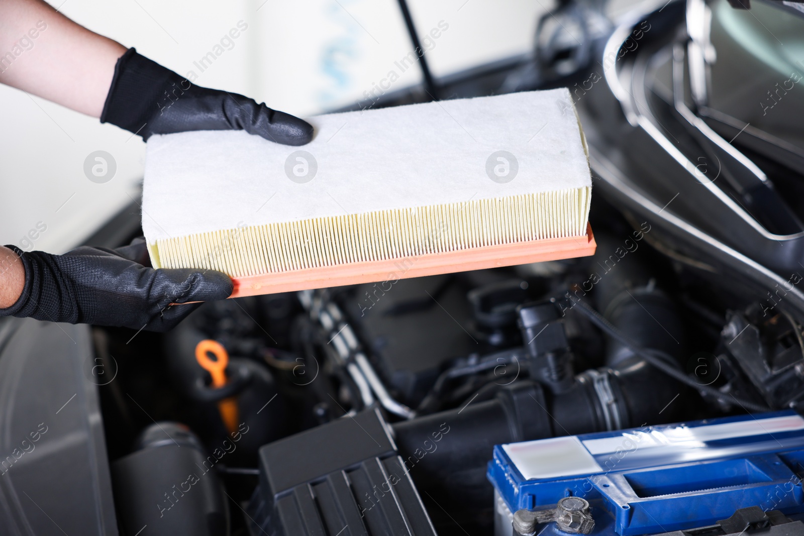 Auto part. Professional mechanic with air filter near open hood of car indoors, closeup Photo of Auto part. Professional mechanic with air filter near open hood of car indoors, closeup