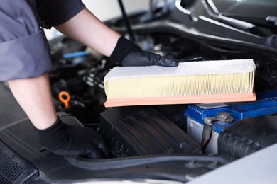 Photo of Auto part. Professional mechanic with air filter near open hood of car indoors, closeup