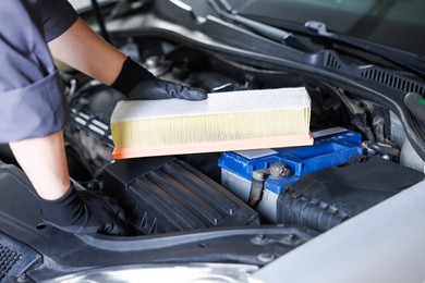 Photo of Auto part. Professional mechanic with air filter near open hood of car indoors, closeup