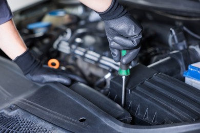Photo of Auto parts. Professional mechanic with screwdriver fixing car indoors, closeup