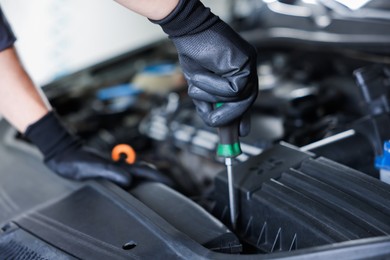 Photo of Auto parts. Professional mechanic with screwdriver fixing car indoors, closeup