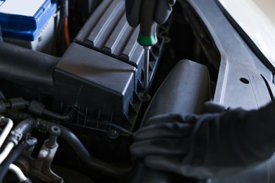 Photo of Auto parts. Professional mechanic with screwdriver fixing car indoors, closeup