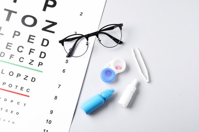 Photo of Vision test chart, glasses, lenses, tweezers and bottles of medical drops on white background, flat lay