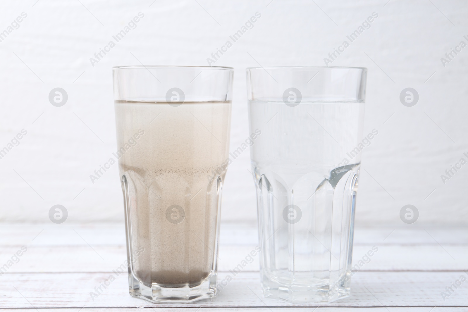 Photo of Glasses with clean and dirty water on white wooden table
