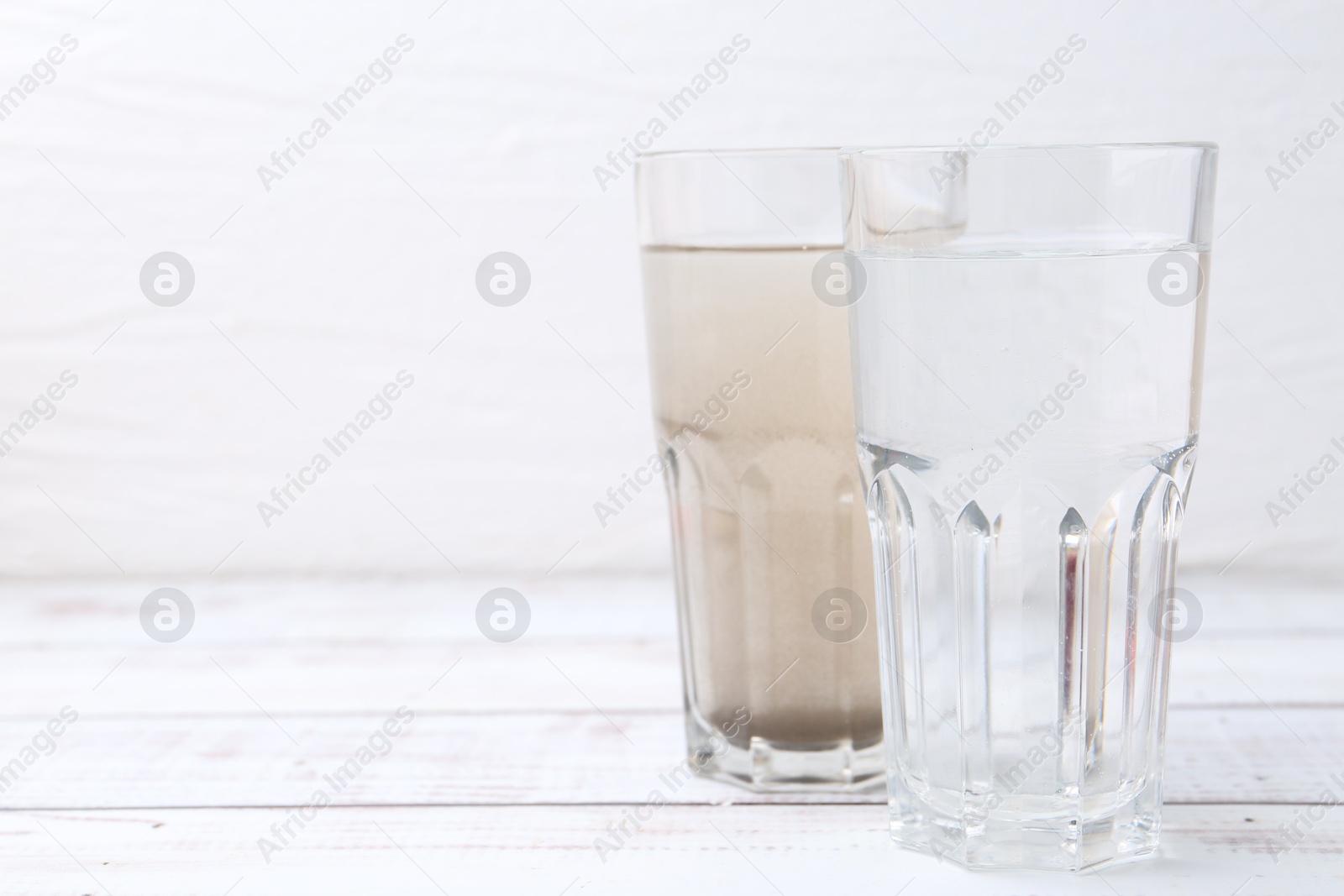 Glasses with clean and dirty water on white wooden table. Space for text Photo of Glasses with clean and dirty water on white wooden table. Space for text