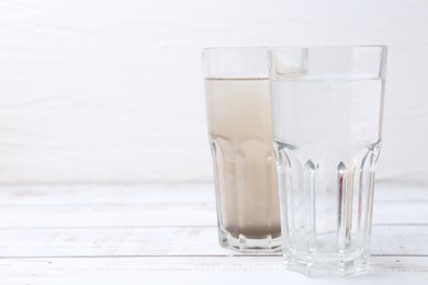 Photo of Glasses with clean and dirty water on white wooden table. Space for text