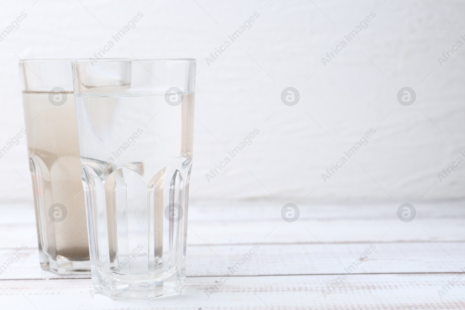Glasses with clean and dirty water on white wooden table. Space for text Photo of Glasses with clean and dirty water on white wooden table. Space for text