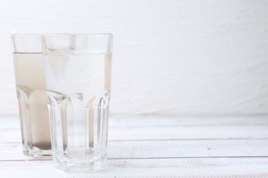 Photo of Glasses with clean and dirty water on white wooden table. Space for text