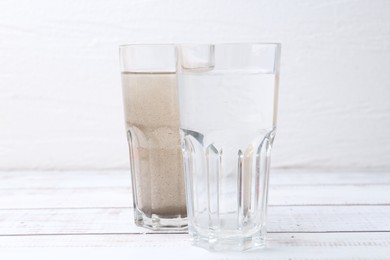 Photo of Glasses with clean and dirty water on white wooden table