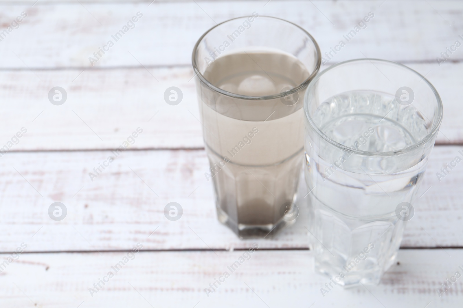 Glasses with clean and dirty water on white wooden table. Space for text Photo of Glasses with clean and dirty water on white wooden table. Space for text