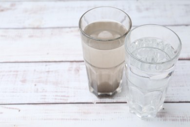 Photo of Glasses with clean and dirty water on white wooden table. Space for text