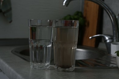Photo of Glasses with clean and dirty water near sink indoors