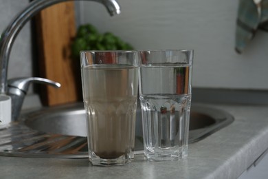 Photo of Glasses with clean and dirty water near sink indoors