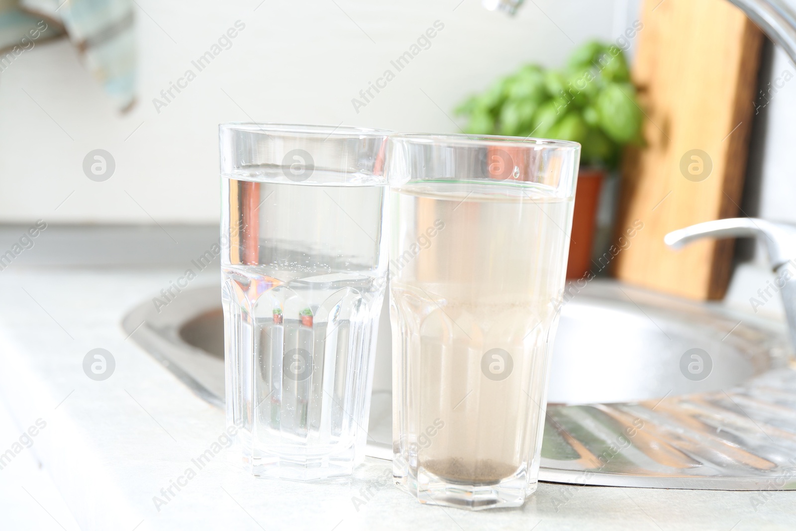 Glasses with clean and dirty water near sink indoors Photo of Glasses with clean and dirty water near sink indoors