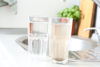 Photo of Glasses with clean and dirty water near sink indoors