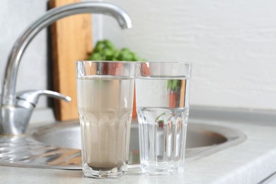 Photo of Glasses with clean and dirty water near sink indoors