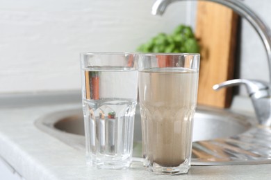 Photo of Glasses with clean and dirty water near sink indoors