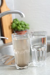 Photo of Glasses with clean and dirty water near sink indoors