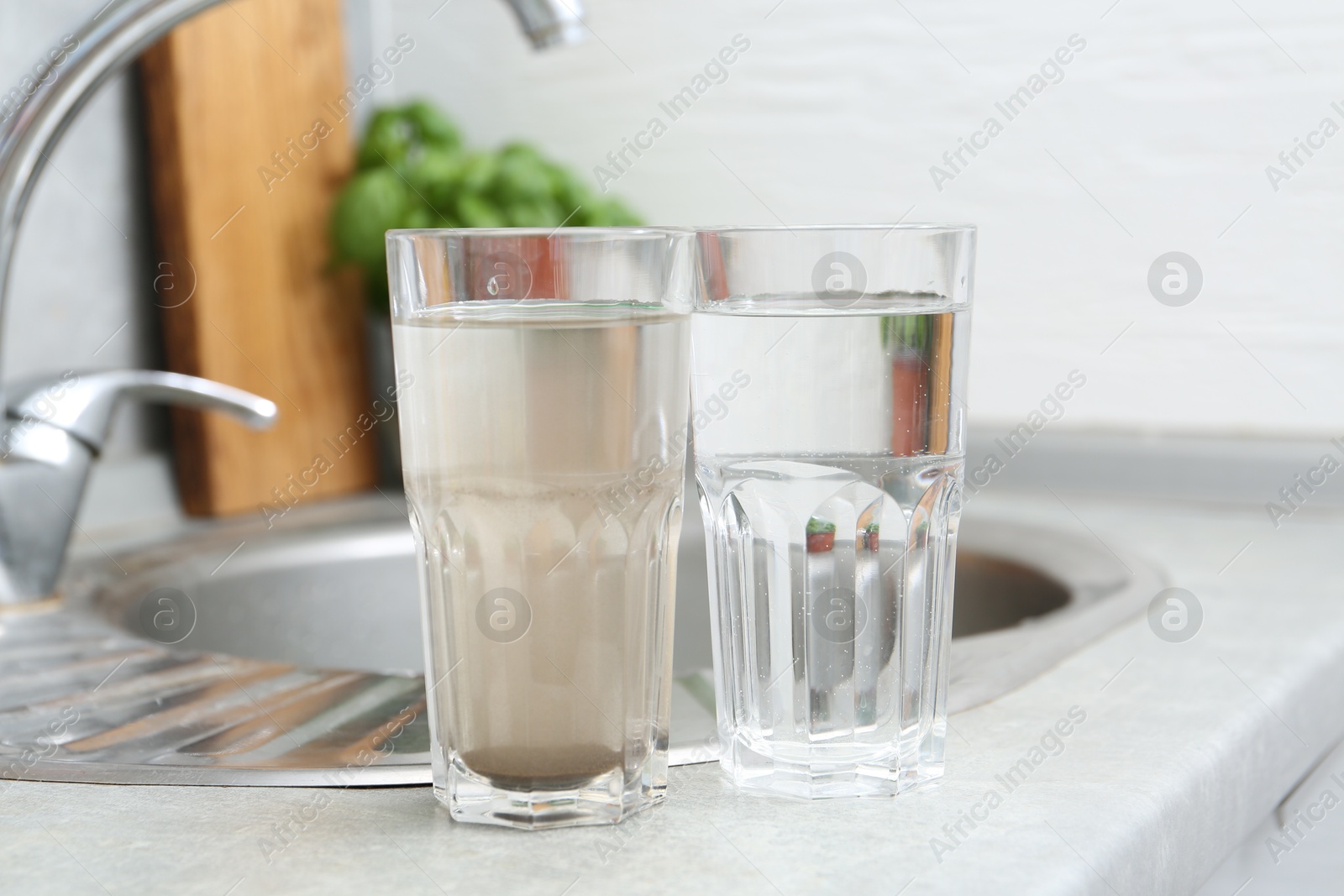 Glasses with clean and dirty water near sink indoors Photo of Glasses with clean and dirty water near sink indoors