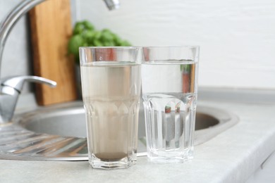 Photo of Glasses with clean and dirty water near sink indoors