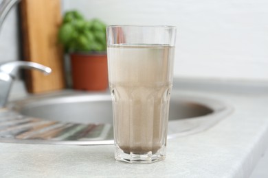 Photo of Glass with dirty water near sink indoors