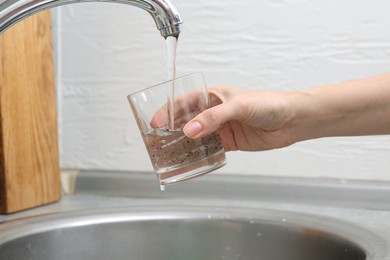 Photo of Woman filling glass with dirty tap water indoors, closeup