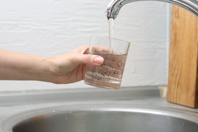 Photo of Woman filling glass with dirty tap water indoors, closeup