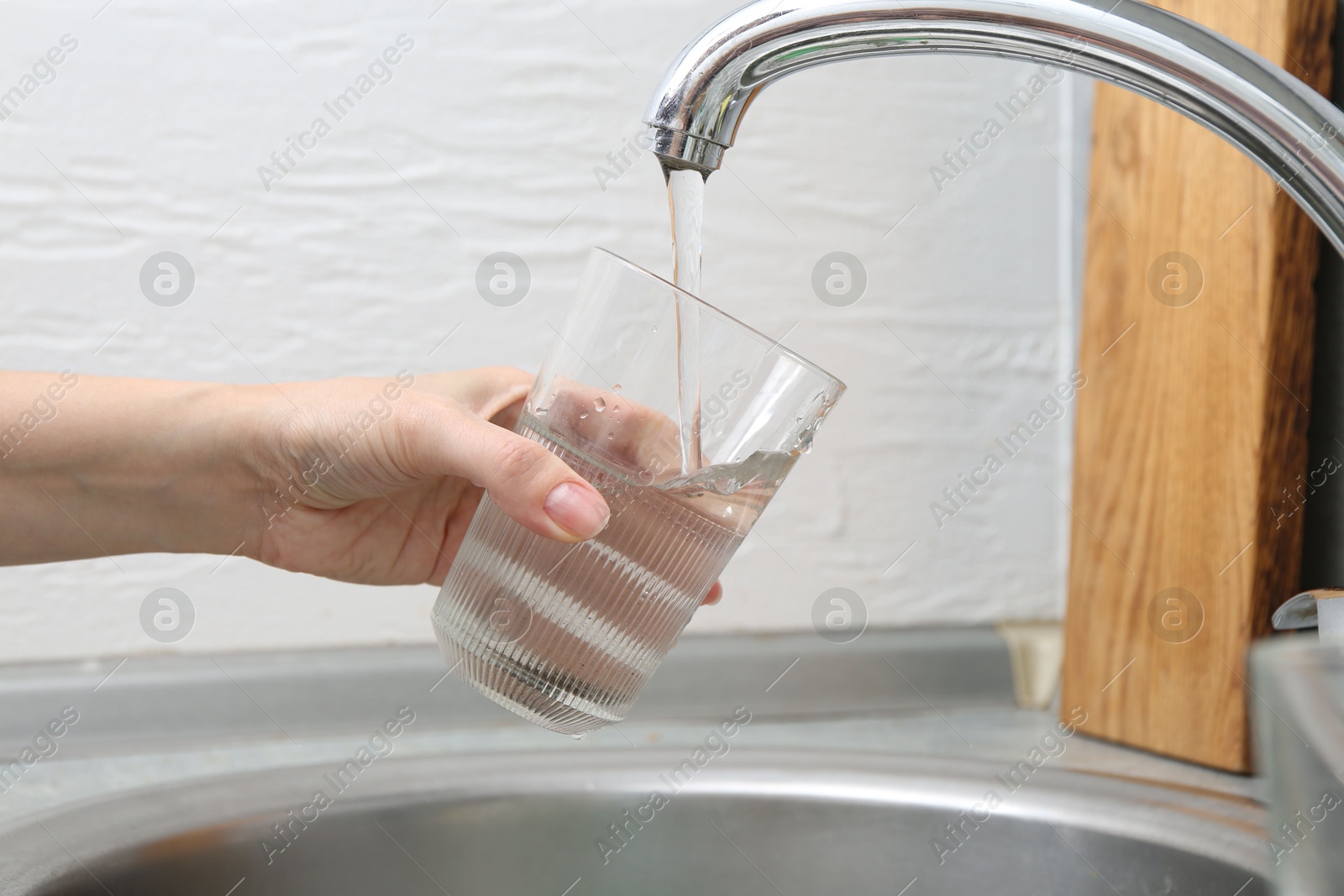 Woman filling glass with dirty tap water indoors, closeup Photo of Woman filling glass with dirty tap water indoors, closeup