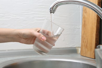 Photo of Woman filling glass with dirty tap water indoors, closeup