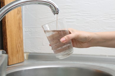Photo of Woman filling glass with dirty tap water indoors, closeup