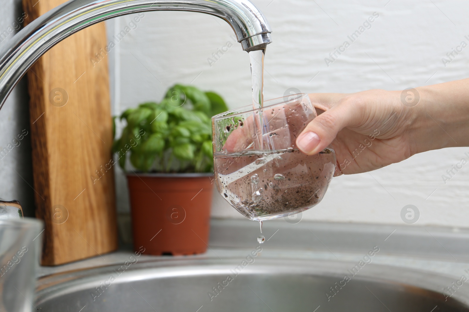 Woman filling glass with dirty tap water indoors, closeup Photo of Woman filling glass with dirty tap water indoors, closeup