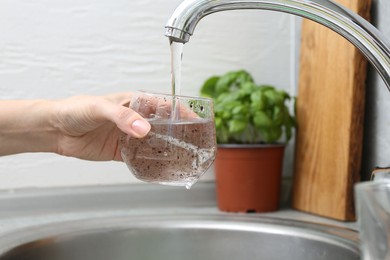Photo of Woman filling glass with dirty tap water indoors, closeup
