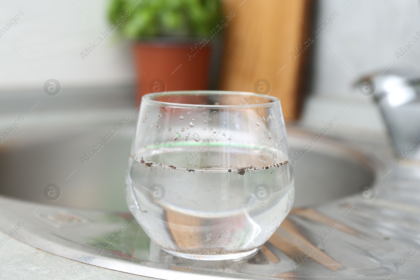 Glass with dirty water near sink indoors Photo of Glass with dirty water near sink indoors