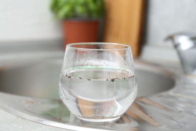 Photo of Glass with dirty water near sink indoors