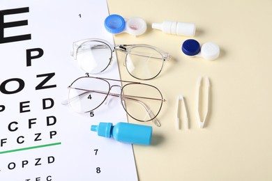 Photo of Vision test chart, glasses, tweezers, lenses and bottles of medical drops on beige background, above view