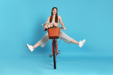 Photo of Smiling woman riding bicycle with basket of flowers against light blue background