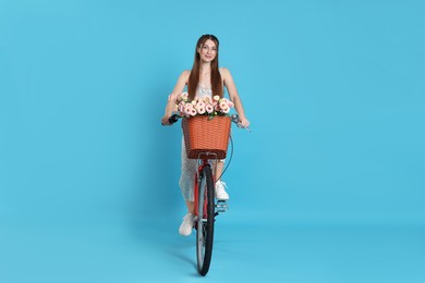 Photo of Beautiful woman riding bicycle with basket of flowers against light blue background