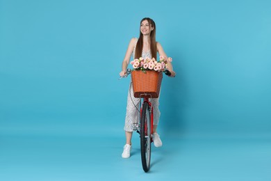 Photo of Smiling woman riding bicycle with basket of flowers against light blue background