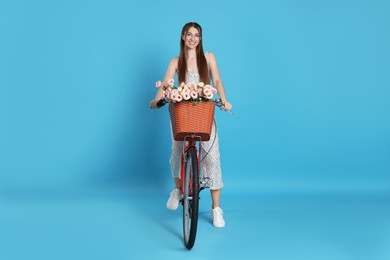 Photo of Smiling woman riding bicycle with basket of flowers against light blue background