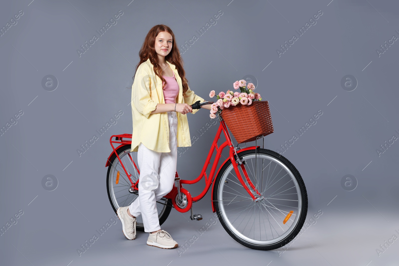 Beautiful teenage girl and bicycle with basket of flowers against grey background Photo of Beautiful teenage girl and bicycle with basket of flowers against grey background