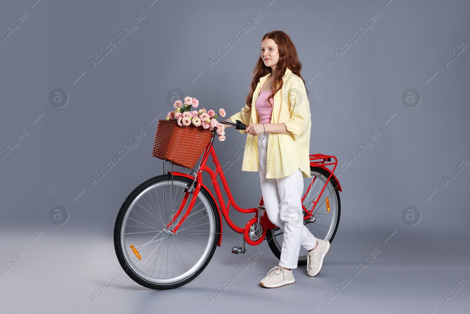 Photo of Beautiful teenage girl and bicycle with basket of flowers against grey background