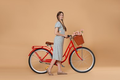 Photo of Smiling woman in dress and bicycle with basket of flowers on beige background