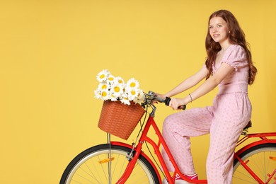 Photo of Smiling teenage girl riding bicycle with basket of flowers against yellow background