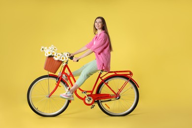 Photo of Smiling woman riding bicycle with basket of flowers against light green background