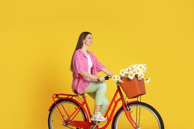Photo of Smiling woman riding bicycle with basket of flowers against yellow background