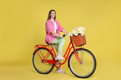 Photo of Smiling woman riding bicycle with basket of flowers against light green background